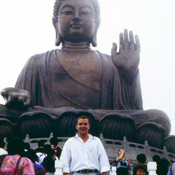 a young man stands in front of a huge statue of the Buddha