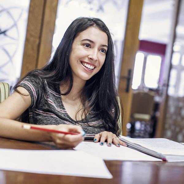 A dark haired woman looks up from where she has been writing out her class schedule and smiles at the person across the table. 