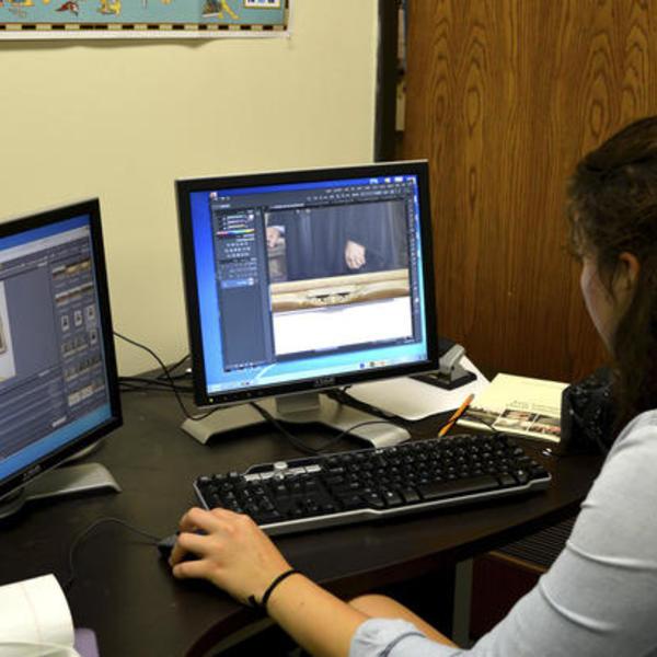 A dark haired young woman works at a computer sorting images.