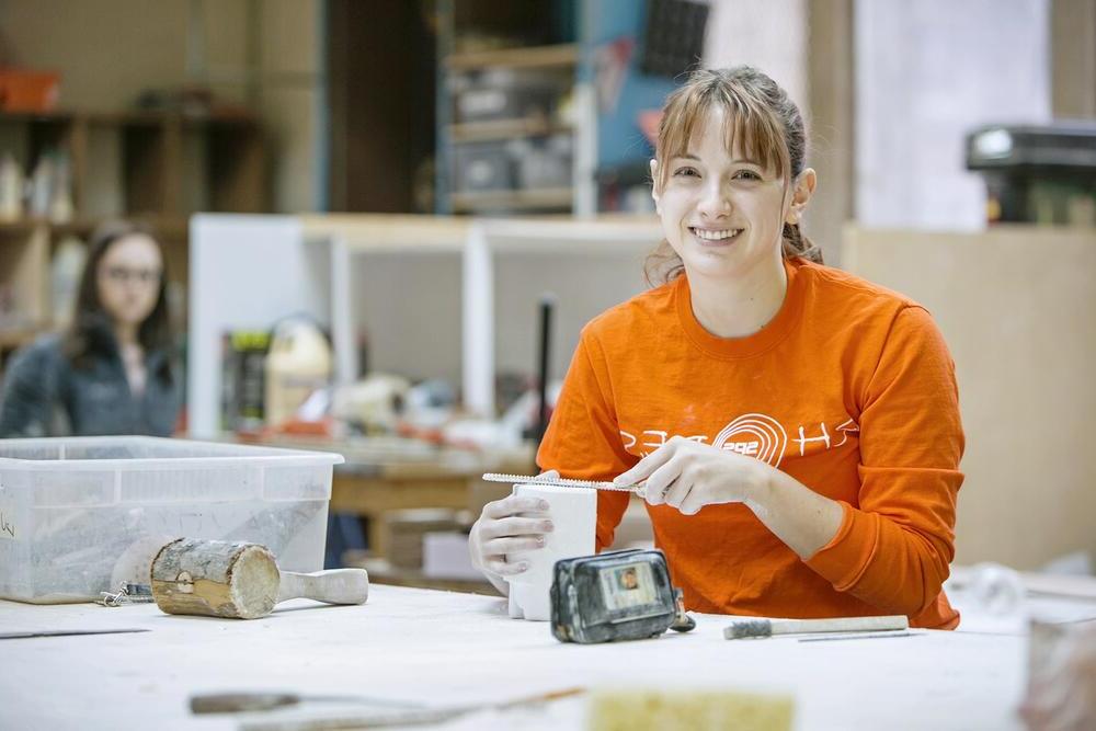 A young woman in an orange shirt files down the end of a mold.
