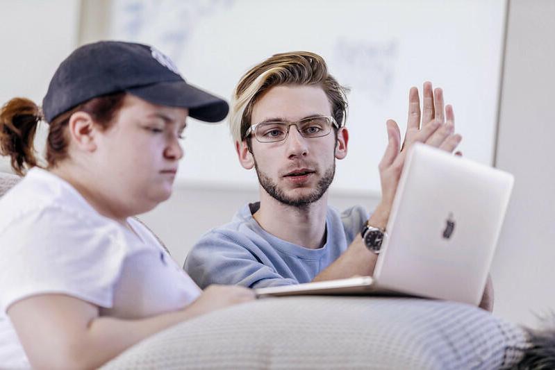 a male student helps another student on a laptop