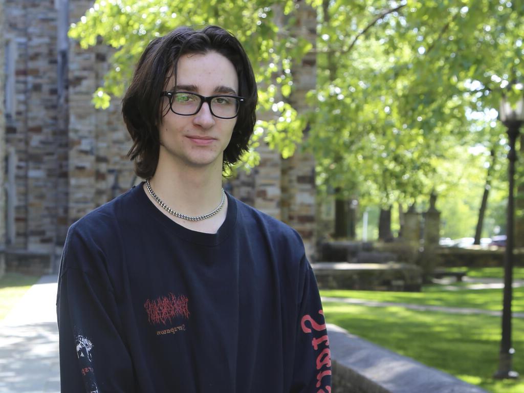 a young man with glasses and dark hair stands on campus