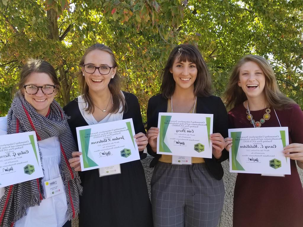 four college students holding up certificates of achievement